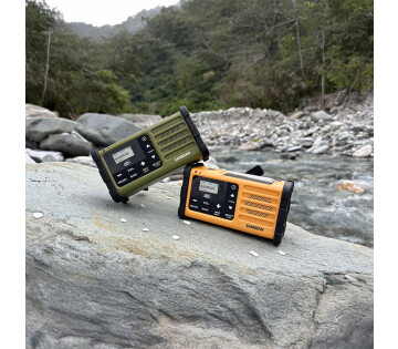 Sangean SDR-800DAB noodradio groen en geel in natuur bij rivier, robuuste noodradio voor outdoor gebruik.