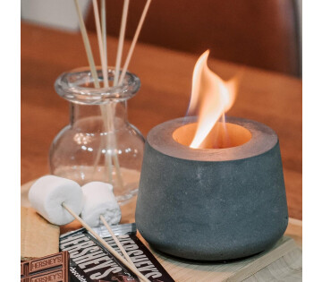 Grijze bio-ethanol tafelhaard naast geurstokjes en marshmallows voor een sfeervol interieurmoment.